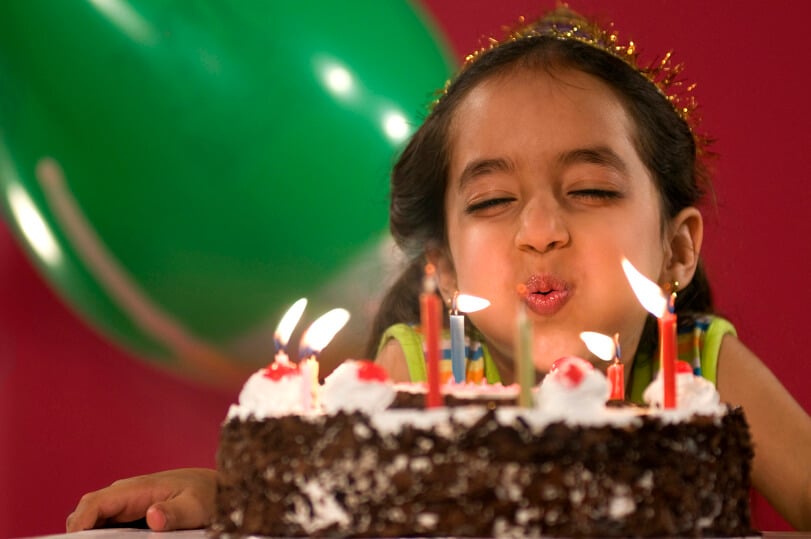 Kleines Mädchen pustet gerade die langen, dünnen Kerze auf ihrem Kuchen aus