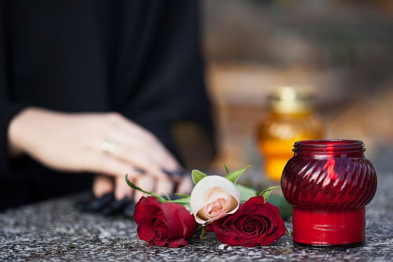 Rote Kerze im Glas mit Rosen zur Trauer um den verstorbenen